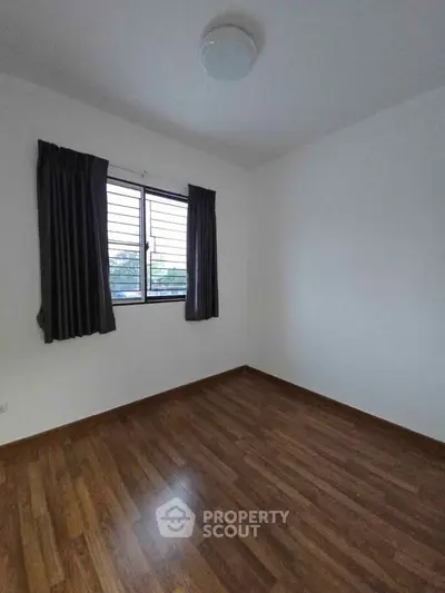 Spacious empty room with wooden flooring and large window, ideal for customization.