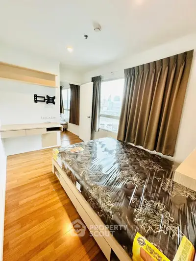 Modern bedroom with wooden flooring and large windows offering city views, featuring a mounted TV bracket and stylish curtains.
