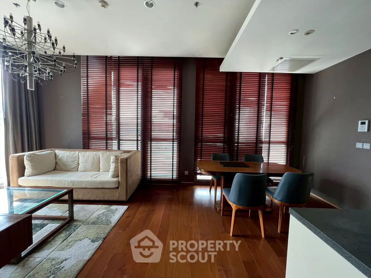 Luxurious living room with elegant wooden flooring and modern furniture, featuring a stylish chandelier and large windows.