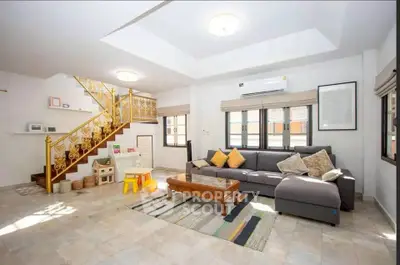 Spacious living room with modern decor and natural light, featuring a cozy sofa and elegant staircase.