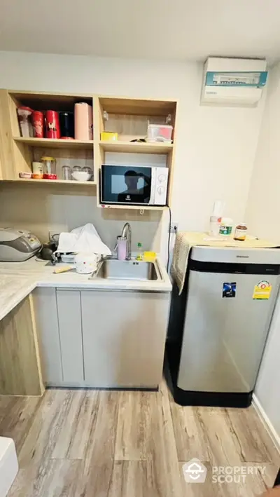 Compact kitchen with modern appliances and wooden cabinetry, featuring a microwave and refrigerator.