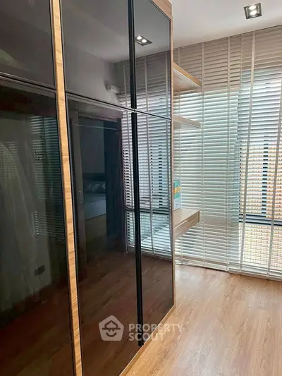 Modern bedroom with sleek black wardrobe and large windows with blinds, offering ample natural light.