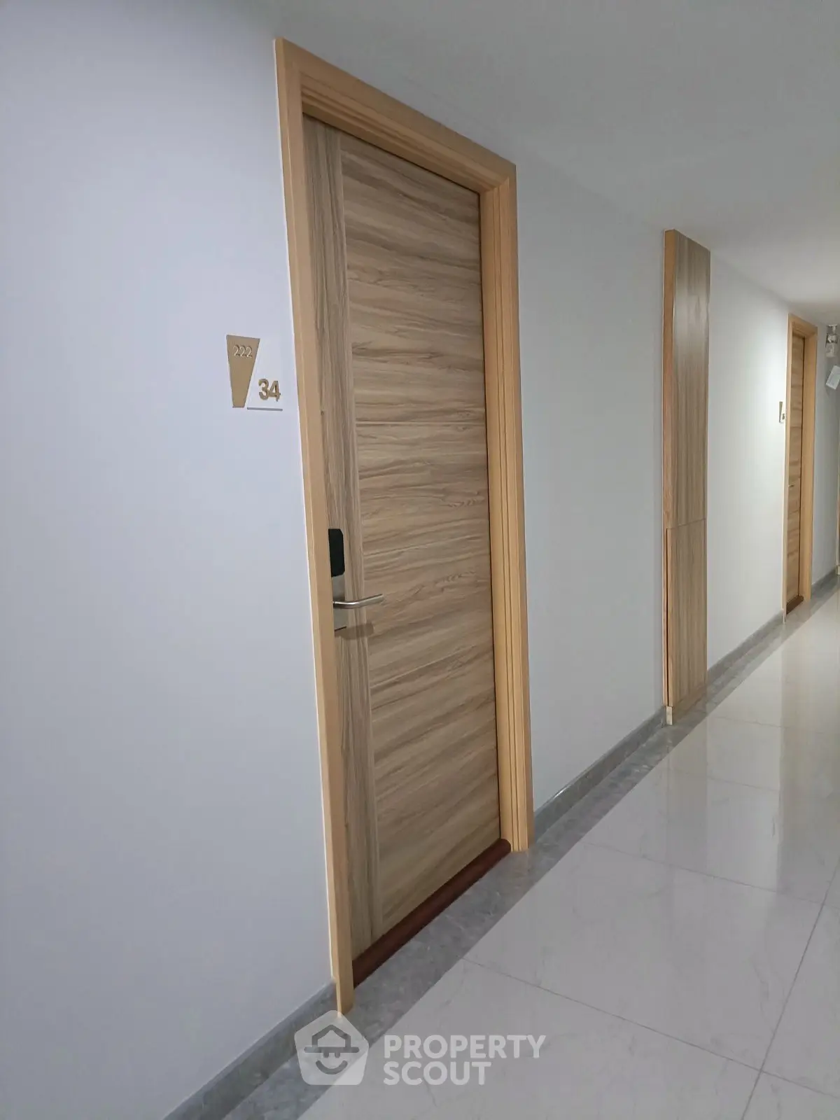 Modern apartment hallway with sleek wooden doors and polished flooring.