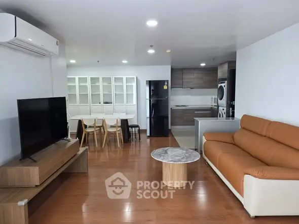 Spacious modern living room with open kitchen, featuring sleek furniture and wooden flooring.
