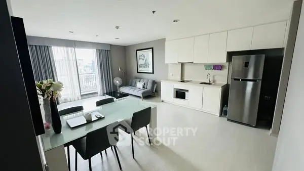 Modern open-layout living room with kitchen and dining area, featuring sleek furniture and natural light.