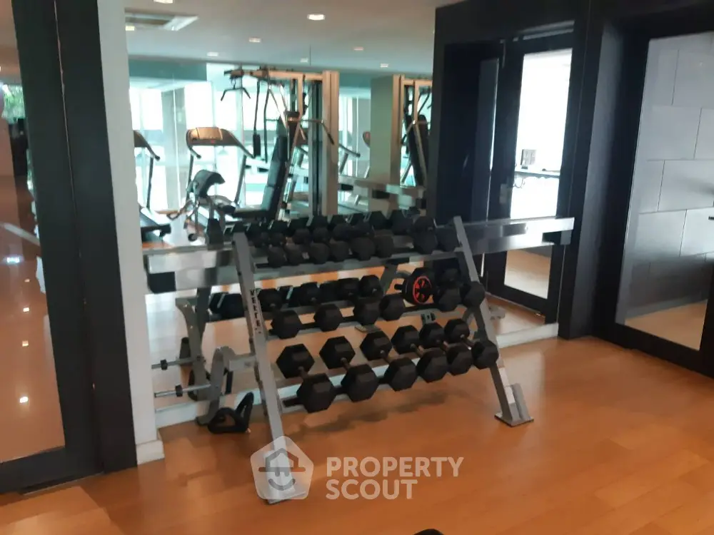 Modern gym with mirrored walls and dumbbell rack in luxury apartment complex