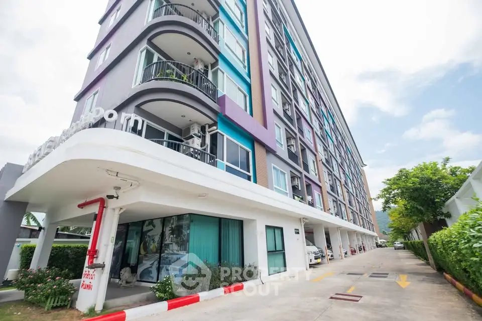 Modern multi-story apartment building with colorful facade and parking area.