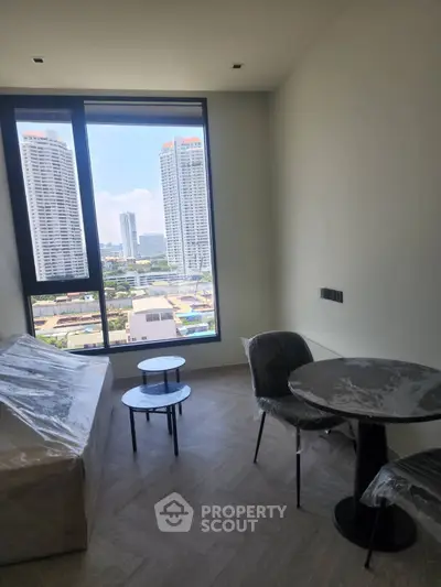 Modern living room with city view, featuring sleek furniture and large window for natural light.
