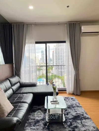 Modern living room with city view, featuring sleek black leather sofa and stylish decor.