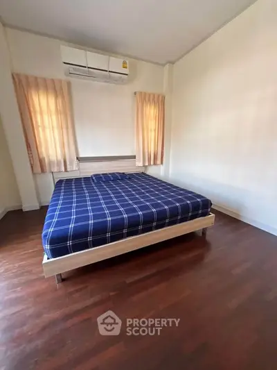 Spacious bedroom with wooden flooring and modern air conditioning unit.