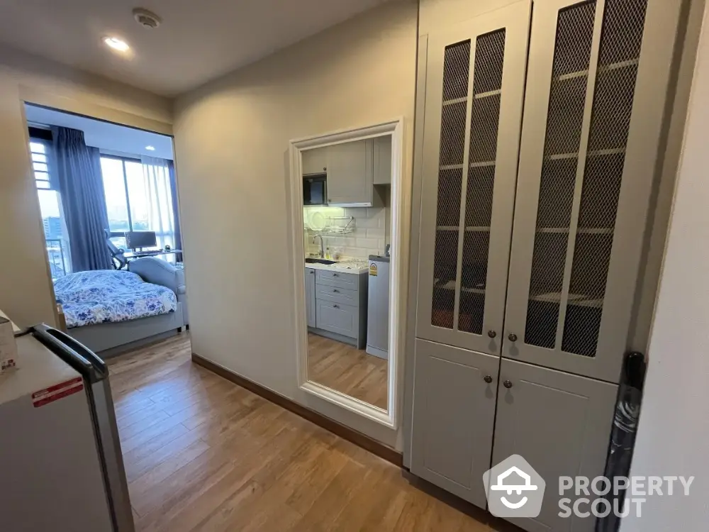 Modern apartment hallway with wooden flooring and built-in storage leading to a cozy bedroom with city view.