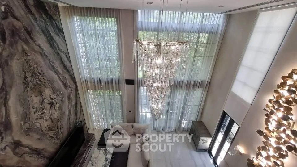 Luxurious high-ceiling living room with elegant chandelier and floor-to-ceiling windows.