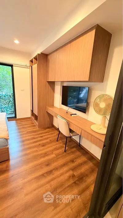 Modern bedroom with built-in desk and TV, featuring wood flooring and large window view.