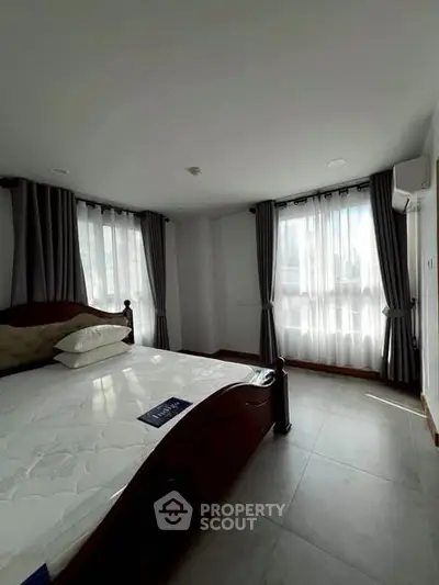 Spacious bedroom with large windows and elegant curtains in a modern apartment.