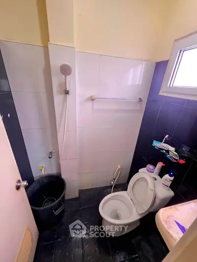 Compact bathroom with shower and toilet, featuring black and white tiles and a small window for natural light.