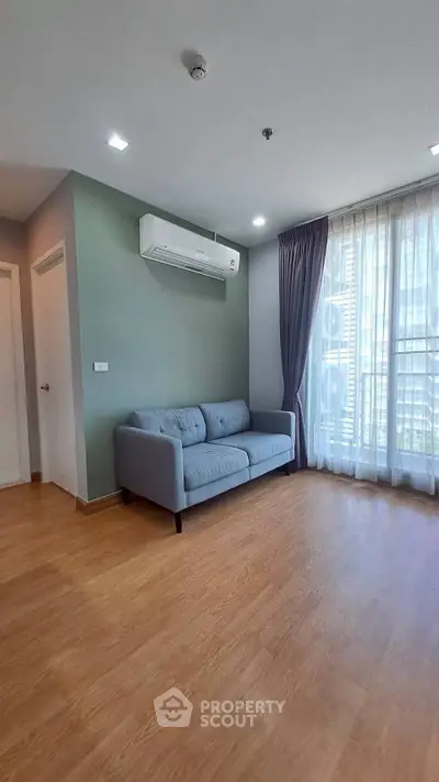Modern living room with sleek sofa and large window, featuring elegant wood flooring and air conditioning.