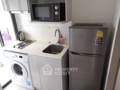 Compact kitchen with modern appliances including washing machine, microwave, and fridge in a cozy apartment.