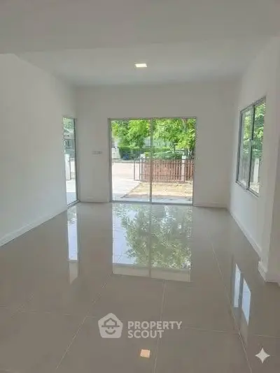 Spacious empty room with glossy tiled floors and large windows offering natural light and garden view.