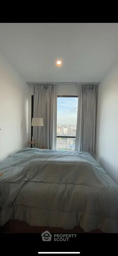 Cozy bedroom with a stunning city view through large window, perfect for relaxation.