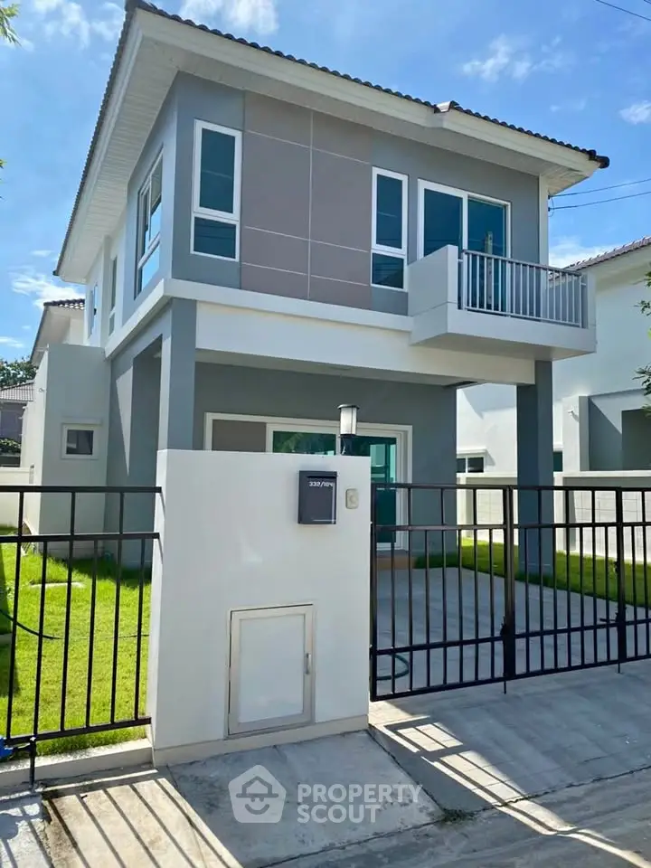 Modern two-story house with balcony and gated entrance in sunny neighborhood.