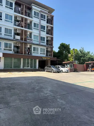 Modern apartment building with parking area and clear blue sky, showcasing urban living convenience.