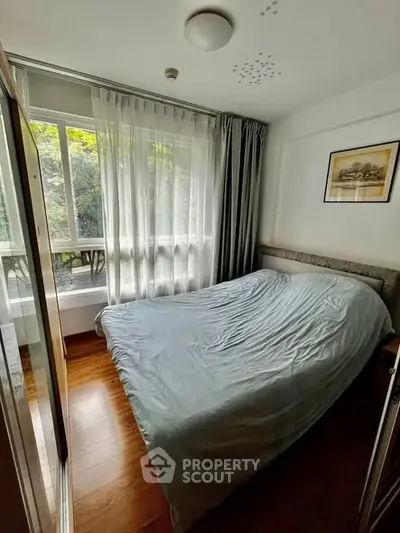 Cozy bedroom with large window and wooden flooring, perfect for natural light lovers.