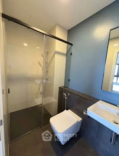 Modern bathroom with sleek design, featuring a glass shower enclosure and wall-mounted sink.