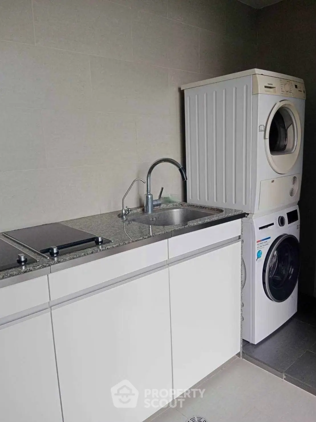 Modern laundry room with stacked washer and dryer, sleek countertop, and built-in sink.