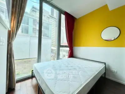 Modern bedroom with large windows and vibrant yellow accent wall in urban apartment.
