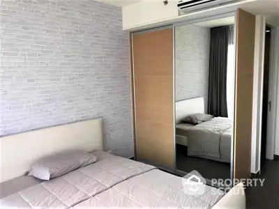 Modern bedroom with large mirrored wardrobe doors reflecting an additional sleeping area, featuring a minimalist design with a white brick accent wall.