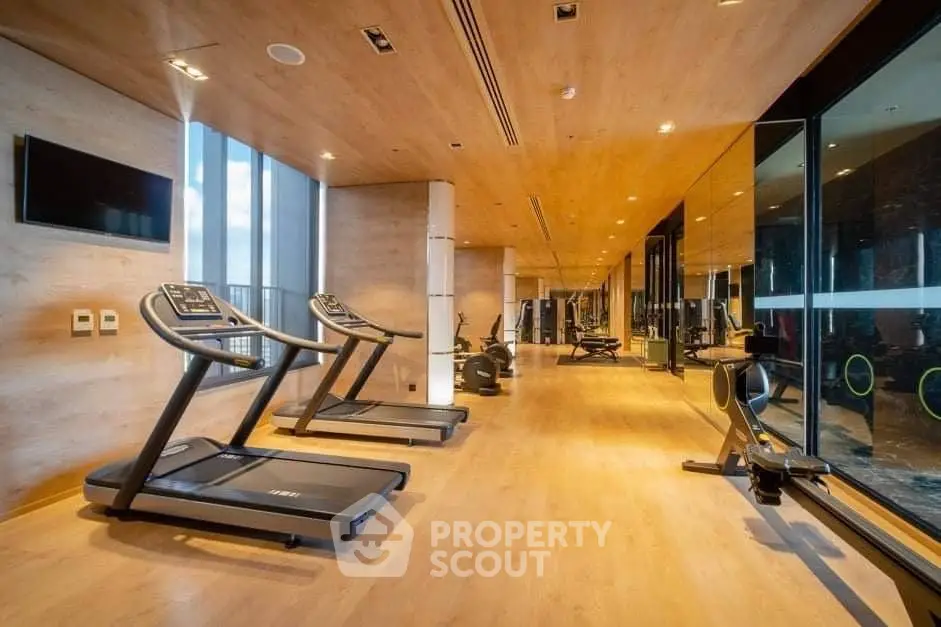 Luxurious gym with modern equipment and wooden flooring in upscale residential building.