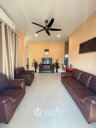 Spacious living room with leather sofas and modern ceiling fan, perfect for relaxation and entertainment.