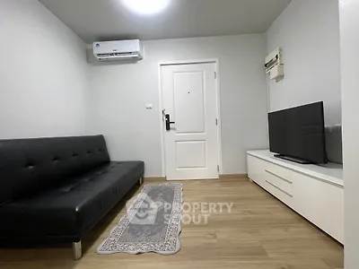 Modern living room with sleek black sofa and flat-screen TV, featuring minimalist decor and wooden flooring.