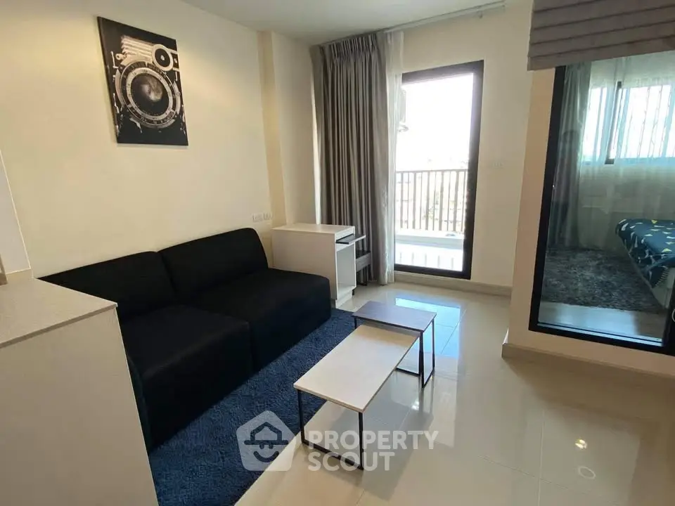 Modern living room with sleek black sofa and stylish decor, featuring a view into the adjacent bedroom.
