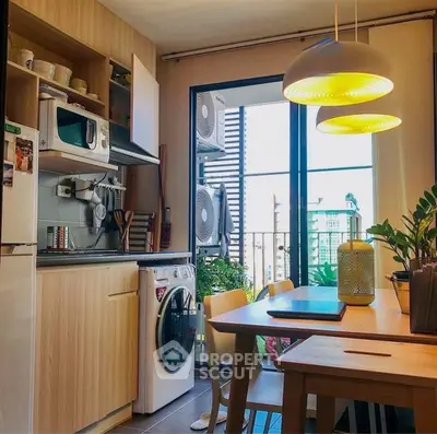Modern kitchen with wooden cabinets, washing machine, and dining area with pendant lights.