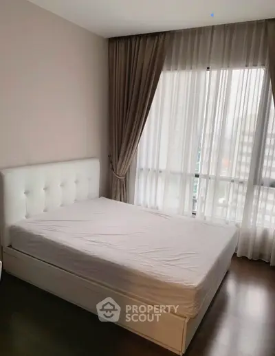 Cozy bedroom with elegant curtains and natural light, featuring a modern white bed frame and hardwood floors.