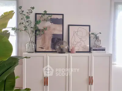 Stylish interior decor with modern art and plants on a white cabinet, perfect for contemporary living spaces.