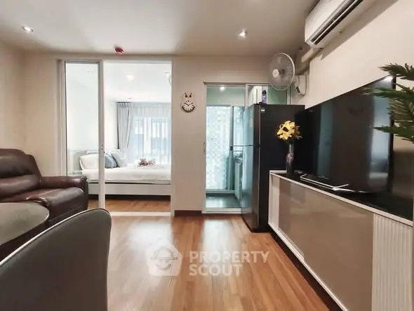 Modern living room with wooden flooring, large TV, and view into a cozy bedroom.