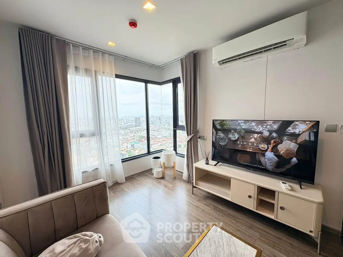 Modern living room with large windows and city view, featuring stylish furniture and a mounted TV.