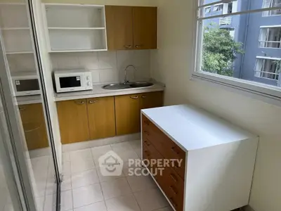Compact kitchen with wooden cabinets and microwave, featuring a large window with a view.