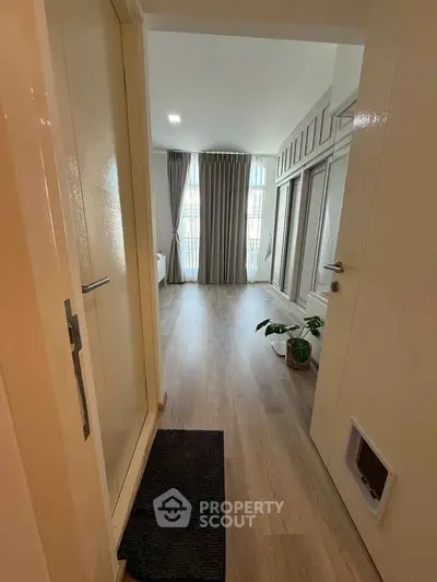 Spacious entryway leading to a bright living area with elegant wood flooring and large windows.