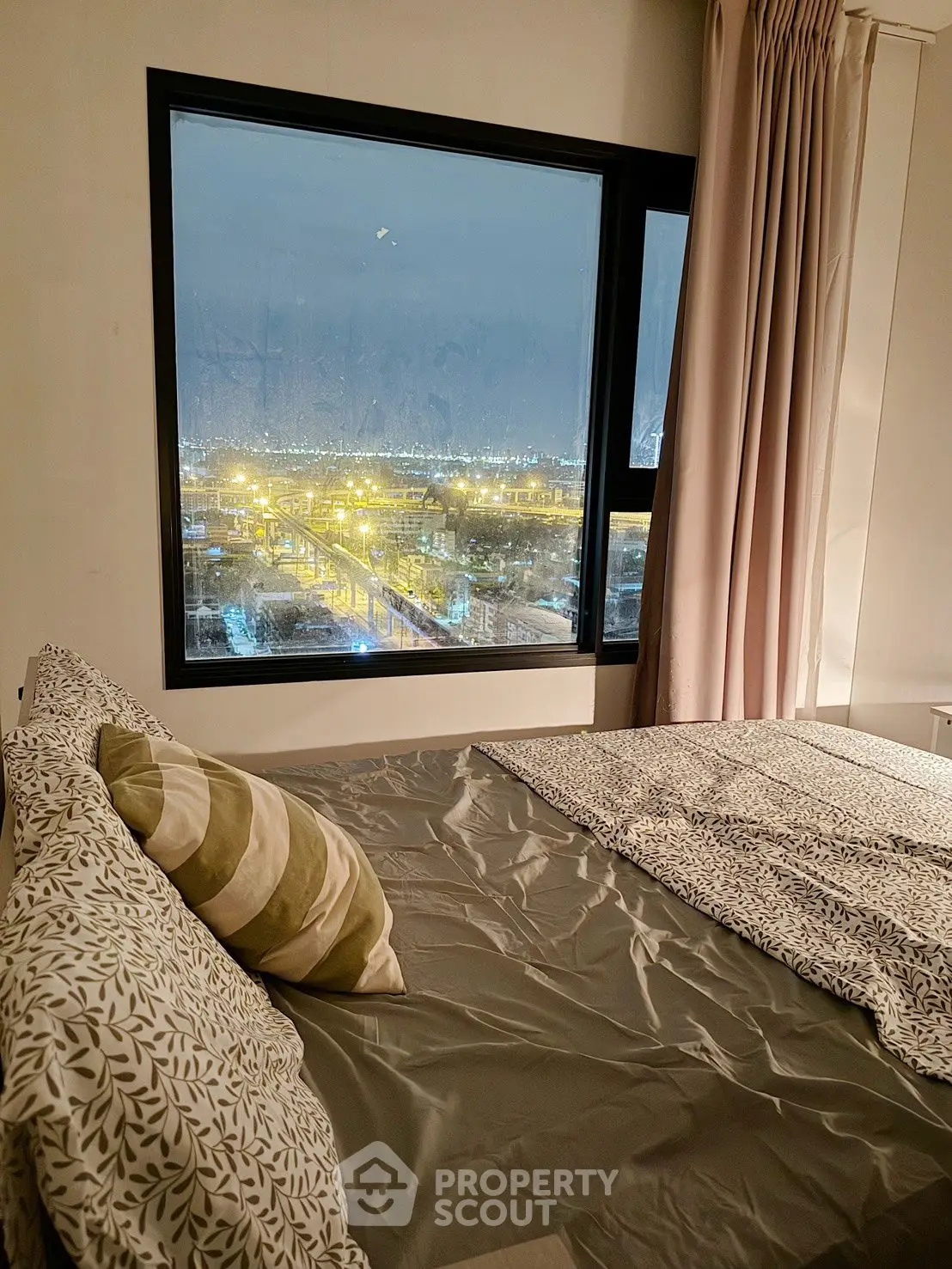 Cozy bedroom with stunning city view through large window at night.