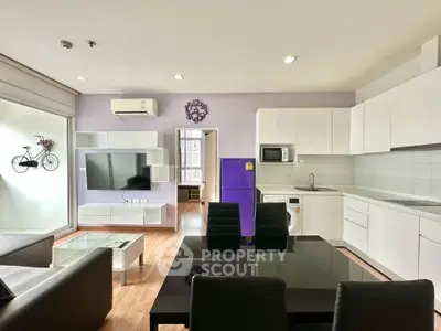 Modern open-layout living room with sleek kitchen and balcony access, featuring stylish decor and ample natural light.