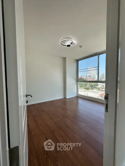 Spacious bedroom with wooden flooring and large window offering city views