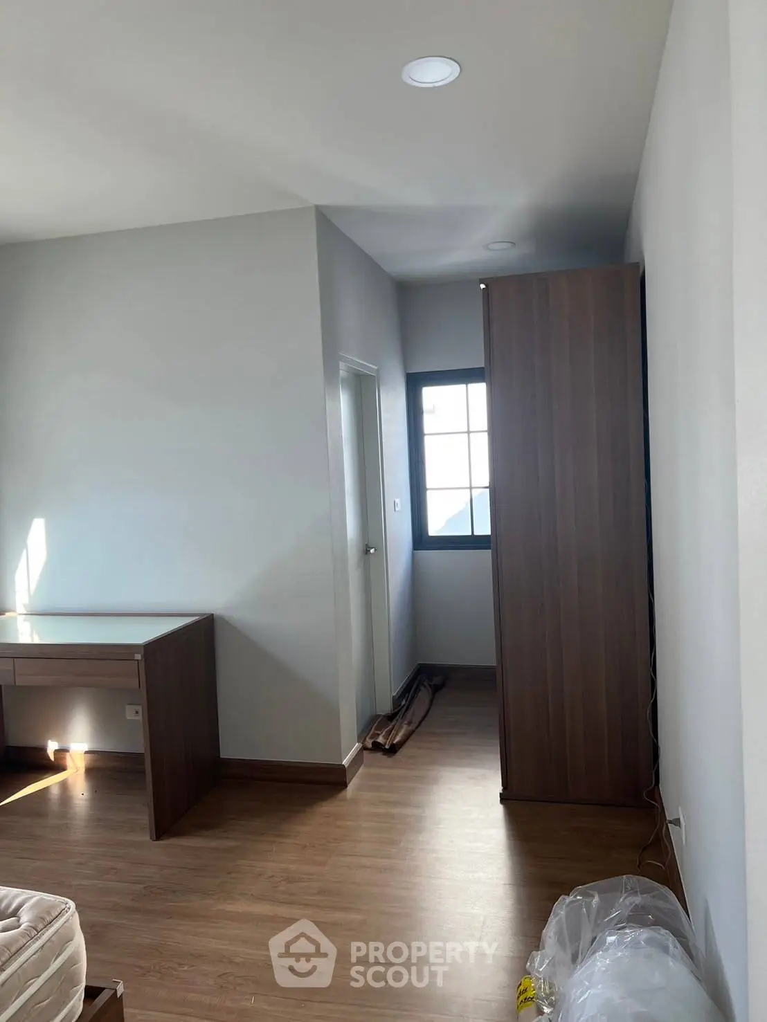 Spacious bedroom with wooden flooring and ample natural light, featuring a desk and wardrobe.