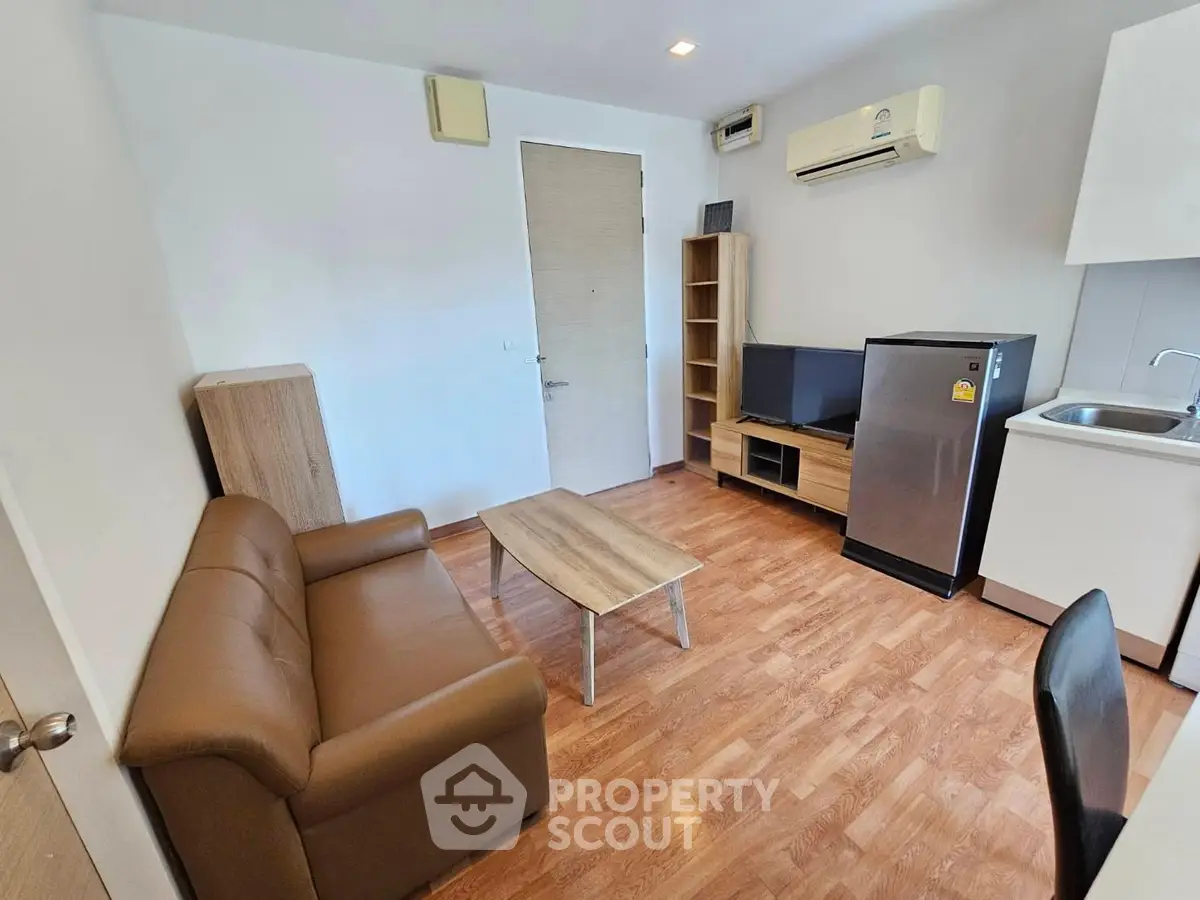 Modern living room with brown sofa, TV, and compact kitchen area in cozy apartment.
