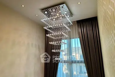 Luxurious modern chandelier in elegant living room with floor-to-ceiling windows and stylish curtains.