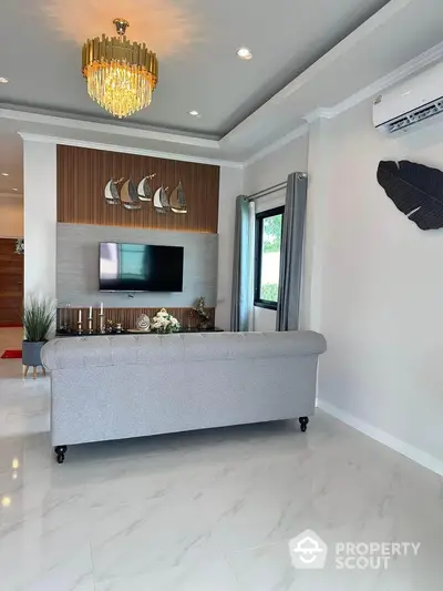 Elegant living room with modern decor, featuring a stylish chandelier, wall-mounted TV, and plush gray sofa.