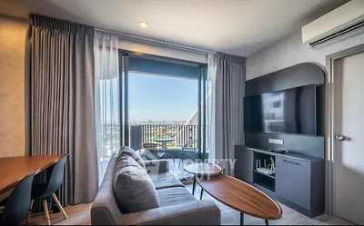 Modern living room with balcony and city view, featuring sleek furniture and natural light.