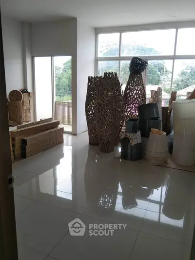 Spacious room with large windows and wicker decor, offering a serene view of greenery.